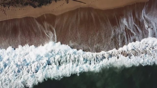 Aerial view of large turquoise waves crashing against at the seashore and people walking on a sand. Stock. Beautiful landscape.
