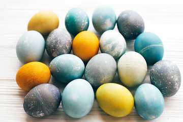 Happy Easter greeting card. Stylish Easter eggs on white wooden background. Modern easter eggs painted with natural dye in yellow,blue,green,grey marble colors.
