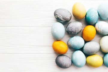 Stylish Easter eggs flat lay on white wooden background with space for text. Modern easter eggs painted with natural dye in yellow,blue,green,grey colors. Happy Easter greeting card