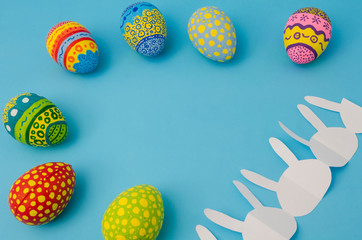 Colorful decorated eggs and white bunny paper chain on blue background. Easter Day decoration
