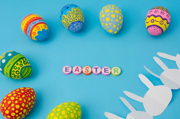 Colorful decorated eggs, white bunny paper chain and Easter made from colorful letters on blue background. Easter Day decoration