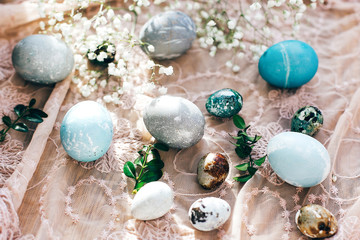 Fototapeta na wymiar Stylish Easter eggs with spring flowers and green buxus branches on rustic fabric in sunny light on wood. Modern colorful eggs painted with natural dye. Happy Easter, greeting card