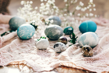 Happy Easter, greeting card. Stylish Easter eggs with spring flowers and green buxus branches on rustic fabric in sunny light on wood. Modern colorful eggs painted with natural dye.