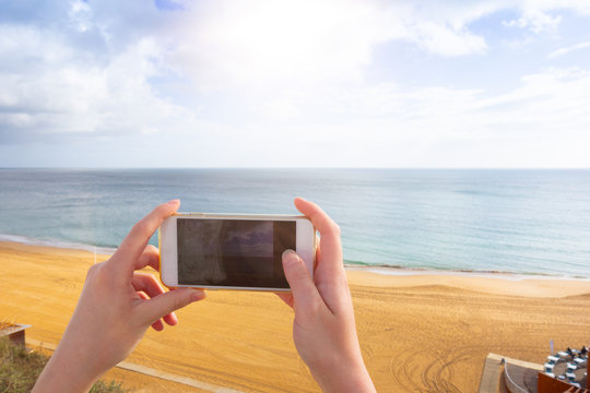 woman taking pictures at the beach with her smartphone