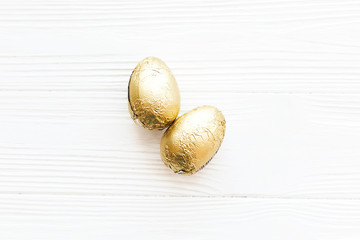Stylish Easter eggs in golden foil on white wooden background flat lay  with space for text. Modern chocolate gold easter eggs. Happy Easter. Greeting card. Holiday gift