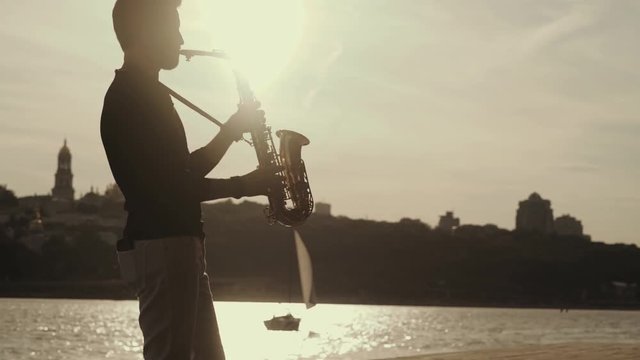 Saxophone player or saxophonist performing sax against sunset