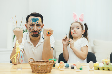 Funny father and daughter painted not only eggs but also each other, preparing for Easter holiday and pleased with the resul of thir work, demonstarate it to the camera, behaving foolishly and making