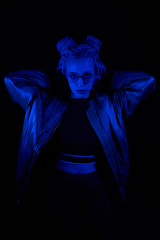 beautiful girl in the light of neon colored lamps light blue wearing glasses on black background