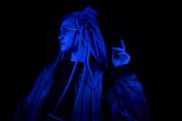 beautiful girl in the light of neon colored lamps light blue wearing glasses on black background