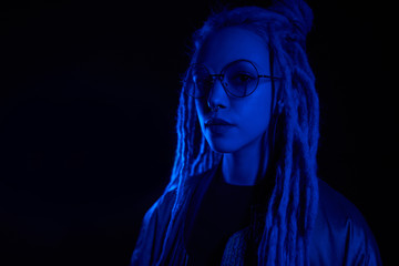 beautiful girl in the light of neon colored lamps light blue wearing glasses on black background