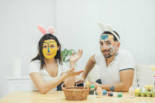 Mother and father painted their faces instead of easter eggs. They are looking at the camera with childish face expression. Foolish behavior. Paint and color.