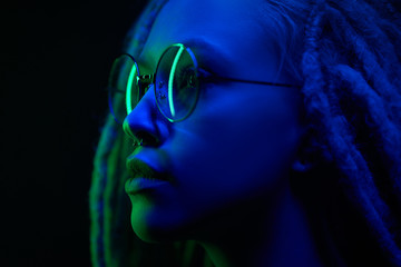 beautiful girl in the light of neon colored lamps light blue green on black background wearing glasses