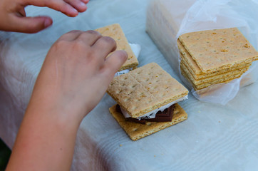 Smore's, a delicious sweet treat with roasted marshmallow, graham cracker and chocolate. Young child's hands making a smore that was fixed outdoors over a campfire while camping. Fun creative eating.
