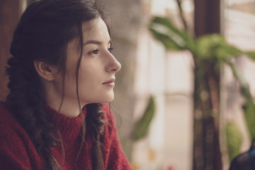 Portrait of young beautiful cute cheerful girl dressed in an orange warm sweater and sitting at a table in a cafe at the table near the window