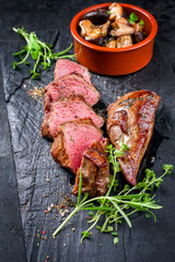 Traditional barbecue aged sliced venison sirloin with mushroom and herbs as closeup on a carbonized old board