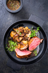 Traditional barbecue aged sliced venison backstrap with mushroom, onions and herbs as top view in a cast-iron pan
