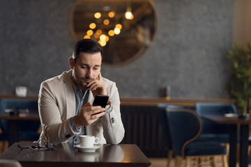 Pensive young businessman reading a text message on smart phone.
