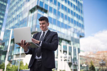 Young businessman using laptop outside against building
