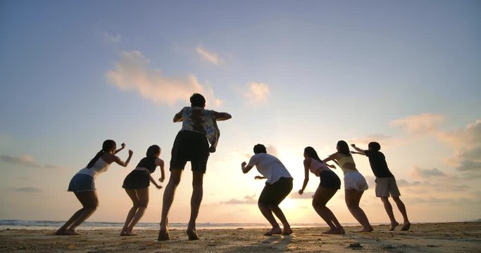 Silhouette of friends jumping on beach during sunset time with happy emotion. 4K resolution. Slow motion shot.