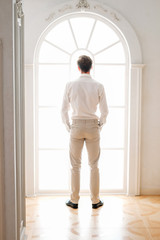 Fototapeta premium Young man standing face to window wearing light beige outfit
