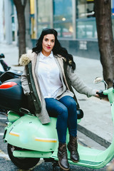 Brunette woman riding on a scooter parked on the street posing.