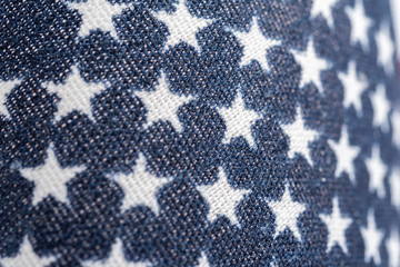A macro shot of white stars with blue background of the American flag printed on a loosely woven fabric.