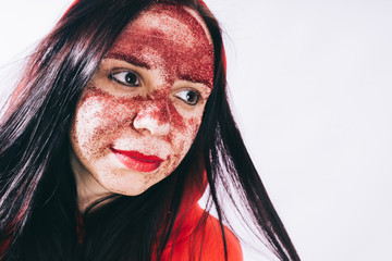 Crazy girl posing in a red hoodie with a painted face. Bizarre portrait with painted face