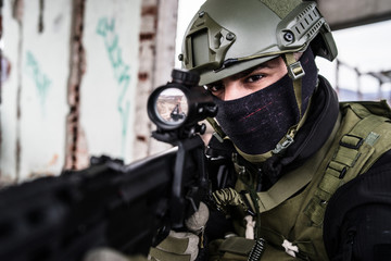 Young Special forces SWAT soldier aiming with assault rifle gun at the ruined building war...