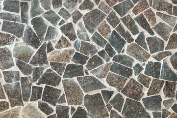 Mosaic wall granite pieces of building in sunny day. Pieces of marble bonded with gray cement.