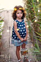 A beautiful little girl with big eyes and dark curly hair gently cares for her goldfish. Festive lights in her hair.