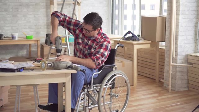Young man disabled in a wheelchair with an electric drill is engaged in repair