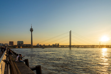 Outdoor scenery of people walk and sit for enjoy nice atmosphere at promenade along riverside of Rhine River during evening sunset time in Düsseldorf, Germany.