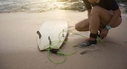 female surfer fastening leash across leg before going to surf