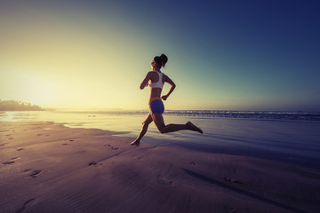 young fitness woman running at sunrise beach
