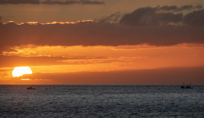 Naklejka na ściany i meble Sunset over the ocean with two small fishing boats