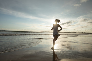 young fitness woman running at sunrise beach