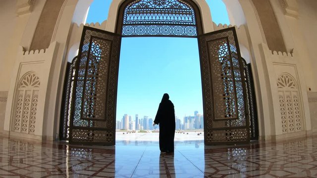 Woman with abaya dress looks at views of skyscrapers of Doha West Bay skyline outdoors State Grand Mosque in Doha, Qatar, Middle East, Arabian Peninsula.