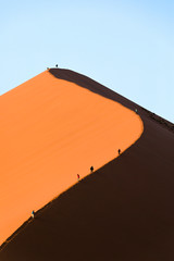 Tourists climb a red sand dune