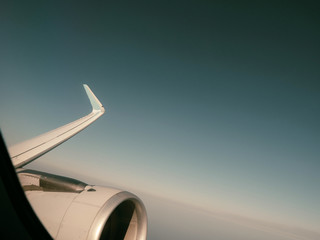 Pale colored film effect over view from window of plane turbine in flight high above clouds in sunlight