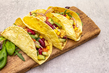 Mexican taco with chicken meat, red beans, fresh vegetables on wooden board. Latin american food, stone background, close up.