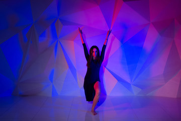 Woman dancing on the background of a beautiful multicolored wall. Sexy slim lonely girl with long black hair in a beautiful dark blue dress. raised hands up, freedom. bright colorful geometry