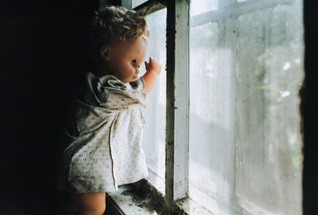 Very scary plastic doll on the background of an old house and a window with a spider web. Halloween and horror. Abandoned and lonely toy. Waiting and peeping.