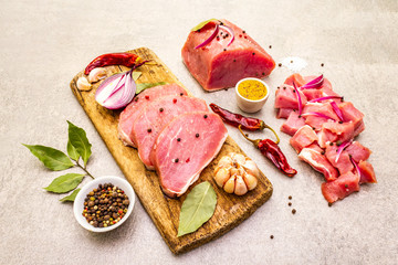 Assortment of slicing raw pork tenderloin with vegetables and spices. Cooking meat background, fresh brisket boneless steak on stone background, close up
