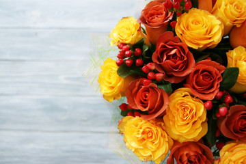 A large beautiful bouquet of yellow and red-orange roses and berries on a gray wooden background....