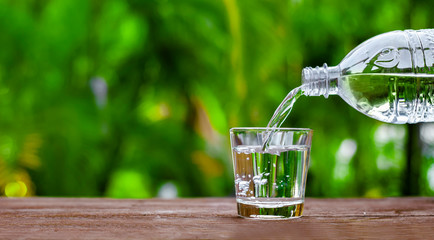 Water in bottle poured into glass on wood with nature background. World Water Day