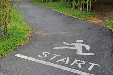 Sign running and word start at point on the asphalt street in park.