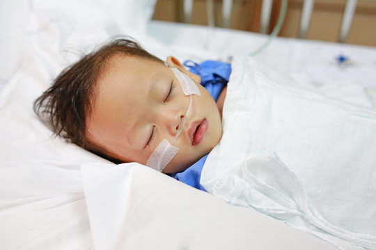 Baby boy age about 1 year old sleeping on patient bed with getting oxygen via nasal prongs to assure oxygen saturation. Intensive care at hospital. Respiratory support.