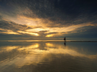 Silhouette couple walking on beach during sunrise ,Reflection of in the calm sea.