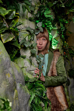 Girl in a green jacket with blond hair near an artificial rock with a grotto. Fabulous photo shoot in the Studio