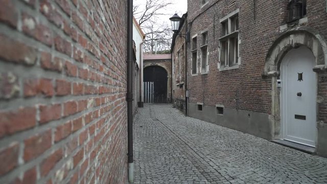 A dead end alleyway in an old European city called Mechelen located in Belgium. A shot of a small cobbled street that is leading to a big closed door.